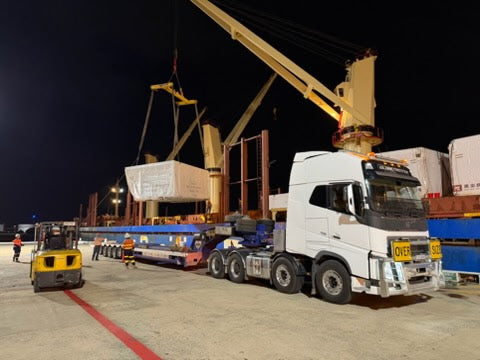 Truck at a dock with a crane lifting cargo at night.