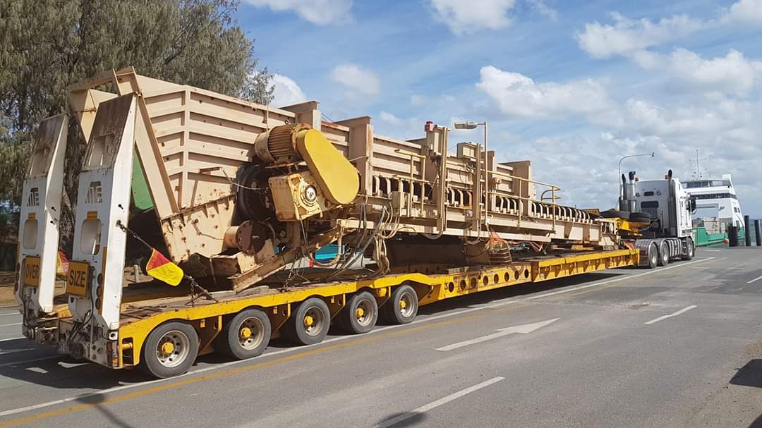 Large truck carrying heavy machinery on a road with a clear sky.