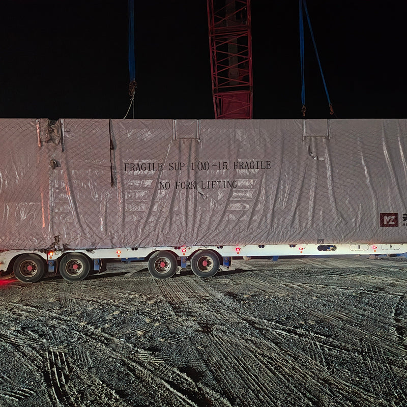 Truck carrying a large wrapped cargo at night with visible branding.